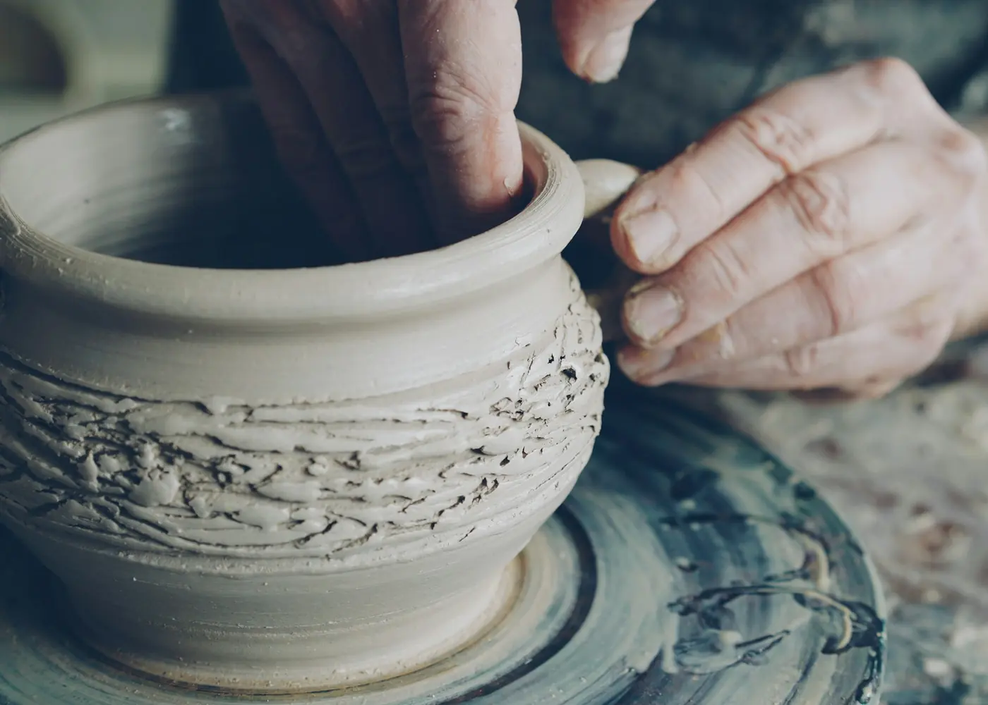 Hands shaping the surface of a clay pot